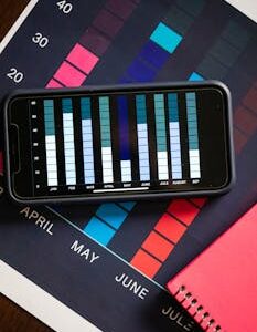Smartphone displaying data chart on a printed financial graph surrounded by a red notebook.